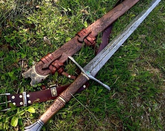 May include: A detailed, ornate sword with a silver blade and a wooden handle, resting on green grass. The sword has a crossguard and is accompanied by a brown leather sheath and belt, both featuring intricate carvings and metal accents.