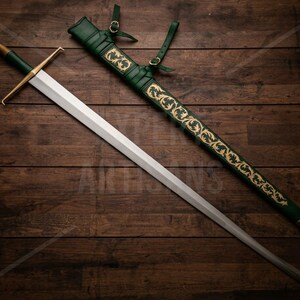 May include: A longsword with a silver-toned blade, a gold-toned crossguard, and a green grip. Beside it lies a matching green scabbard featuring intricate gold-toned floral scrollwork patterns and leather straps with gold-toned buckles.