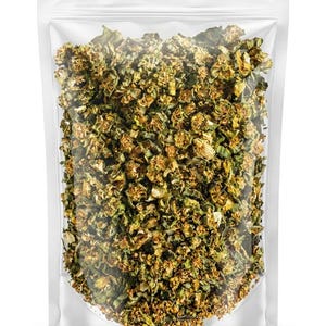 May include: A clear, resealable plastic bag filled with dried, chopped herbs. The herbs are a mix of green and tan, with a textured appearance. The bag is sealed at the top and sits against a white background.