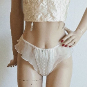 May include: A white satin and lace bustier with a plunging neckline and a matching white tulle panty with a ruffled hem and white polka dots.