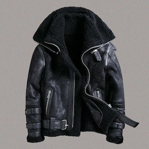 May include: Black shearling leather jacket with a wide collar and multiple zips. The jacket features a buckled belt at the waist and cuffs. The interior is lined with black shearling. A stylish and warm outerwear option.