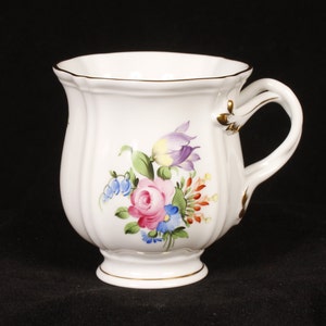May include: White porcelain teacup with a floral design featuring pink, purple, yellow, blue, and red flowers. The cup has a gold rim and a gold handle.
