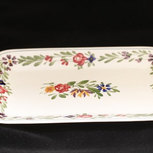 Peut inclure: Un plat de service rectangulaire blanc avec un motif floral. Le bord du plat est décoré d'un motif continu de feuilles vertes, de fleurs roses, rouges et bleues. Le centre du plat présente un motif floral similaire avec un groupe de fleurs rouges, roses et jaunes.