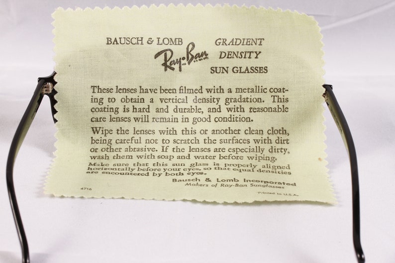 Puede incluir: Gafas de sol Ray-Ban negras con un pa&ntilde;o de limpieza. El pa&ntilde;o tiene el texto "BAUSCH & LOMB Ray-Ban GRADIENT DENSITY SUN GLASSES". El texto del pa&ntilde;o proporciona instrucciones sobre c&oacute;mo limpiar las lentes.