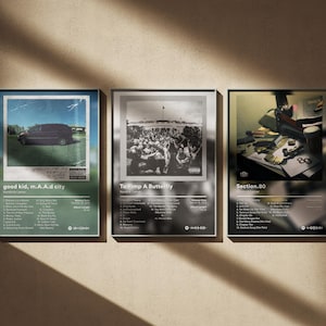 Puede incluir: Tres impresiones enmarcadas de arte de álbum. La primera presenta una furgoneta sobre un fondo verde con el texto "good kid, m.A.A.d city". La segunda es en blanco y negro con una multitud y el texto "To Pimp a Butterfly". La tercera tiene una escena de escritorio y el texto "Section.80".