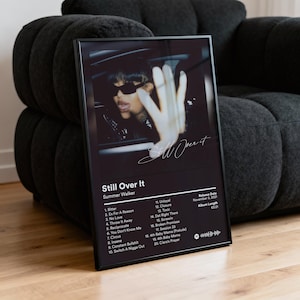May include: Black framed poster featuring the album cover for "Still Over It" by Summer Walker. The image shows a woman in sunglasses with a hand over the car window. The album tracklist and release details are also displayed.