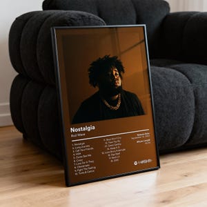 May include: A framed poster featuring Rod Wave's album "Nostalgia." The poster has a brown background with a portrait of the artist. The album's tracklist, release date, and album length are listed in white text.
