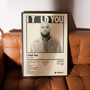 May include: A framed poster featuring the album "I Told You" by Tory Lanez. The poster has a black frame and a cream-colored background. The album cover features a sepia-toned portrait of Tory Lanez. The album's tracklist and release details are also displayed.