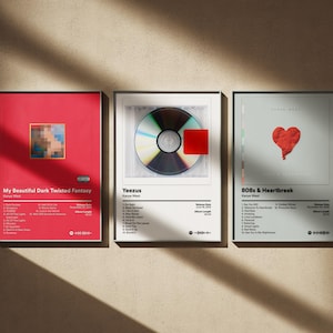 May include: Three framed album art prints. The first is red with the text "My Beautiful Dark Twisted Fantasy" and a pixelated design. The second features a CD and the text "Yeezus". The third has a red heart and the text "808s & Heartbreak".