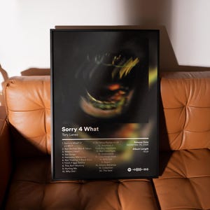 May include: A framed poster featuring the album "Sorry 4 What" by Tory Lanez. The poster has a black frame and displays the album title, tracklist, and release information. The background image is a blurred, abstract design with yellow and green hues.