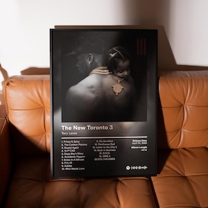 May include: A framed poster featuring the album art for "The New Toronto 3" by Tory Lanez. The artwork is a black and white image of a person with a child, wearing gold jewelry. The poster includes a tracklist and release information.