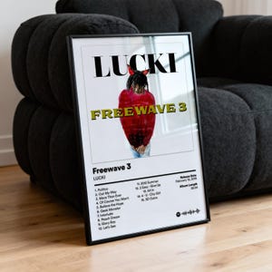 以下が含まれることがあります： LUCKIのアルバム「Freewave 3」のアートワークが描かれたフレーム入りポスター。アーティストが赤と黒の衣装を着ています。アルバムタイトルは黄色で、アーティスト名は大きな黒い文字で書かれています。ポスターは木製の表面に表示されています。