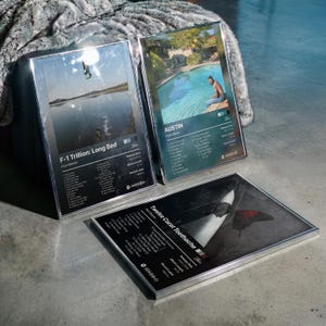 May include: Three framed rectangular posters featuring Post Malone album art for F-1 Trillion: Long Bed, Austin, and Twelve Carat Toothache. Each print displays tracklists, release dates, album lengths, record labels, and Spotify codes in silver frames.