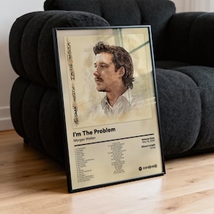 Può includere: Poster incorniciato con l'album "I'm The Problem" di Morgan Wallen. L'opera d'arte include un ritratto dell'artista e una tracklist. Il poster è in una cornice nera e poggia su un divano grigio scuro.