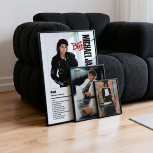 Può includere: Poster incorniciati con copertine di album di Michael Jackson. Il poster "Bad" mostra Jackson con una giacca nera, mentre i poster "Thriller" e "Off the Wall" presentano immagini iconiche. I poster sono esposti contro un divano nero.