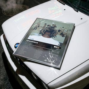 Puede incluir: Un póster rectangular enmarcado que presenta el álbum Xperiment de Ken Carson. La imagen muestra a una persona con rastas desde atrás, una lista de 22 canciones, fecha de lanzamiento 3 de julio de 2020, duración 60:32 y el sello Opium.