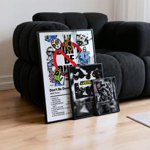 Puede incluir: Tres impresiones artísticas enmarcadas apoyadas contra un sofá negro. La impresión más grande presenta ilustraciones coloridas y el texto "Don't Be Dumb" de A$AP Rocky. También se ven dos impresiones más pequeñas en blanco y negro.
