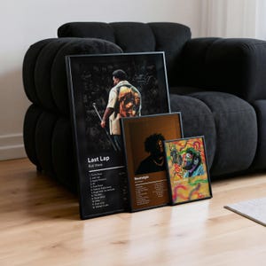 May include: Three framed art prints leaning against a black sofa. The largest print features a man with a microphone, the text "Last Lap" and a tracklist. The other two prints have portraits and text, including "Nostalgia" and "Beautiful Mind".