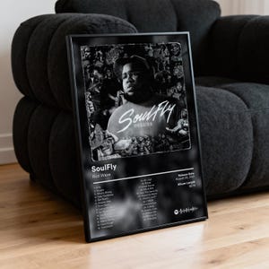 May include: Black and white framed poster featuring the album art for "SoulFly Deluxe" by Rod Wave. The poster includes the album title, artist name, tracklist, release date, and album length. The image is set against a dark background.