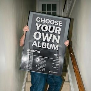 May include: A rectangular black-framed poster featuring the bold white text CHOOSE YOUR OWN ALBUM at the top. Below, it displays placeholders for Album Title, Artist Name, twenty track titles, release date, album length, and record label.