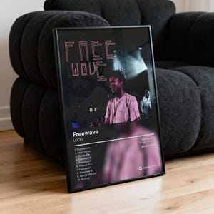 以下が含まれることがあります： ラッキーのアルバム「Freewave」をフィーチャーした黒いフレームのポスター。ポスターは黒い背景に「FREE WAVE」と書かれたピンク色のテキストがあります。ポスターの画像はステージ上の人物を示しています。アルバムのトラックリストは画像の下に表示されています。