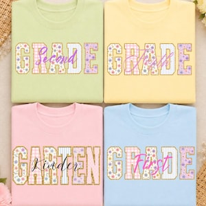May include: Four crewneck sweatshirts in light green, yellow, pink, and light blue. Each features the word GRADE or GARTEN in large block letters with floral and striped patterns, overlaid with cursive text reading Second, Fourth, Kinder, and First.