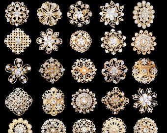 May include: Twenty-four gold-toned brooches with clear rhinestone embellishments. The brooches feature a variety of intricate designs, including floral, geometric, and abstract patterns.