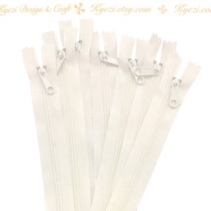 Könnte beinhalten: Eine Ansammlung cremefarbener Reißverschlüsse mit silberfarbenen Zippern und Zähnen. Die Reißverschlüsse sind fächerförmig vor weißem Hintergrund angeordnet. Der Text "Kyezi Design & Craft" und eine Website-Adresse sind sichtbar.