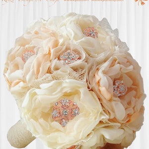 May include: A bridal bouquet composed of cream and peach fabric flowers, embellished with sparkling rhinestone and rose gold brooches. The handle is wrapped in cream fabric. The text "Kyzei Design & Craft" is visible at the top.