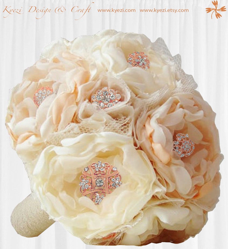 May include: A bridal bouquet composed of cream and peach fabric flowers, embellished with sparkling rhinestone and rose gold brooches. The handle is wrapped in cream fabric. The text "Kyzei Design & Craft" is visible at the top.