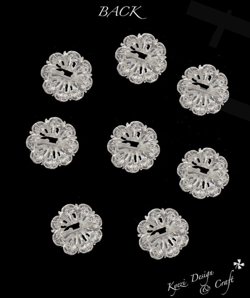 May include: Eight clear plastic flower-shaped buttons with a decorative design. The buttons have a hole in the centre and are arranged in a grid pattern on a black background.