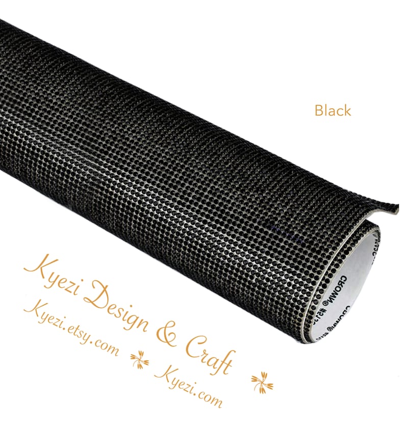 May include: A roll of black adhesive-backed rhinestone sheet. The sheet is covered in small, black rhinestones. The sheet is rolled up and the adhesive side is visible.