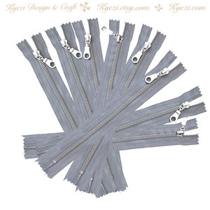 May include: A pack of 12 silver zipper pulls with gray tape. The zippers are arranged in a fan shape.