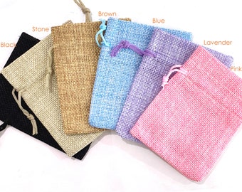 May include: Six small burlap drawstring bags in various colors, including black, brown, stone, blue, lavender, and pink. The bags are arranged in a row from left to right, with the black bag on the left and the pink bag on the right.