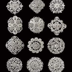 May include: Twelve silver brooches with rhinestone embellishments. The brooches are in various shapes and sizes, ranging from 3 to 3.5 cm.