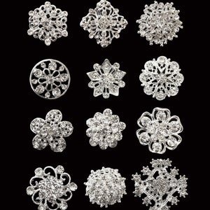 May include: Twelve silver brooches with crystal embellishments in various designs, including floral, geometric, and snowflake patterns. The brooches are approximately 2 to 2.5 cm in size.