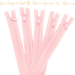May include: Five pink zipper closures, each with a metal slider. The zippers are arranged in a fan shape, with the top of each zipper pointing towards the center.