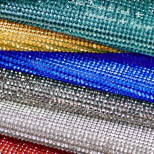 May include: Close-up of five rolls of rhinestone fabric in different colors: teal, gold, blue, silver, and red. The fabric is made of small, round rhinestones.