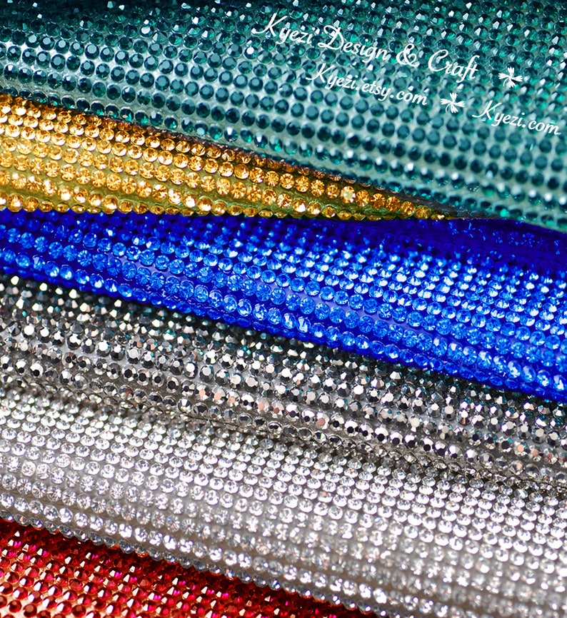 May include: Close-up of five rolls of rhinestone fabric in different colors: teal, gold, blue, silver, and red. The fabric is made of small, round rhinestones.