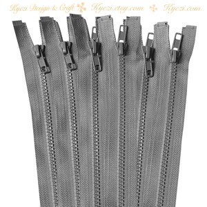 May include: A close-up of a bundle of eight gray zipper closures. The zippers are all closed and have a metal tooth design.