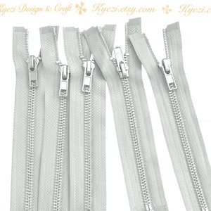 May include: Several silver-toned zippers with white fabric. The zippers are closed and have a metal pull tab. The image includes the text "Kyezi Design & Craft" and "Kyezi.etsy.com".