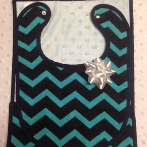 May include: A turquoise and navy blue chevron patterned bib with a white satin bow.