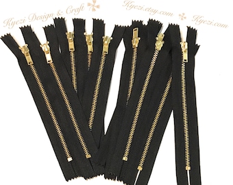May include: Eight black zipper closures with gold metal sliders. The zippers are all the same length and are arranged in a row.