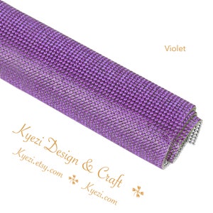 May include: A roll of purple rhinestone mesh fabric. The fabric is covered in small, round rhinestones. The fabric is rolled up and the end of the roll is visible. The text "Violet" is visible in the upper right corner of the image.