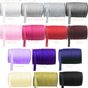 以下が含まれることがあります： 白、ピンク、赤、黒など、さまざまな色のサテンリボンのスプールのセレクション。画像には、色の名前を示すラベルが付いたリボンのスプールが表示されています。 Etsyショップ名とウェブサイトのアドレスが上部に表示されています。