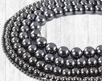 May include: A variety of sizes of gunmetal hematite beads. The beads are round and smooth, and they are arranged in a circle on a white wooden background. The text "Hematite Beads ~Gunmetal~" is at the top of the image. The text "Kyezi Design & Craft www.kyezi.etsy.com www.kyezi.com" is at the bottom of the image.