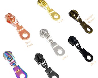 Könnte beinhalten: Sortiment an Reißverschluss-Zierbändern in verschiedenen Farben, darunter Gold, Roségold, Silber, Gunmetal, Schwarz, Antik-Bronze und Regenbogen. Jeder Zipper hat einen runden Ring am unteren Ende.