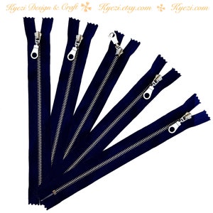May include: Six navy blue zips with silver metal pulls. The zips are arranged in a fan shape.