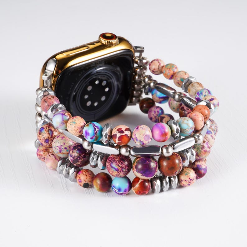 May include: A gold-colored smartwatch with a black face is paired with a beaded bracelet. The bracelet features multiple strands of colorful, round beads in shades of purple, pink, orange, and blue, interspersed with silver-toned metal accents.