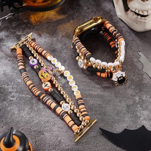 May include: Halloween-themed Apple Watch bands with orange, black, and white beads. One band spells "HALLOWEEN" with white letter beads. Charms include a spider, pumpkin, and other Halloween icons. The watch case is gold.